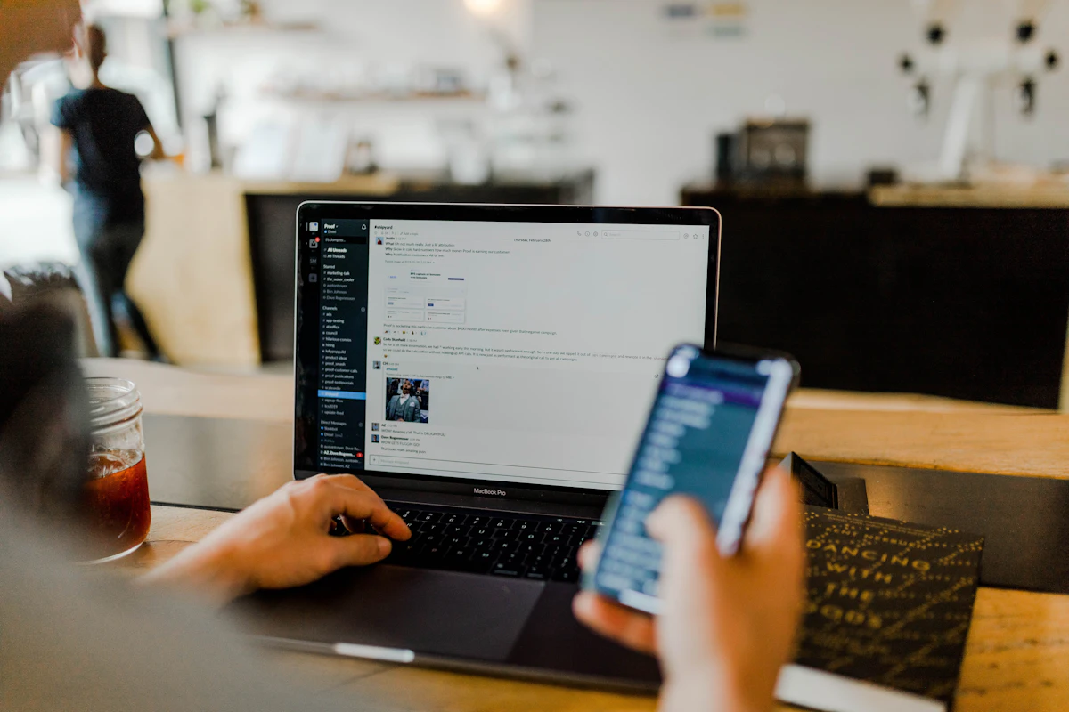 Person working on a laptop while checking a phone